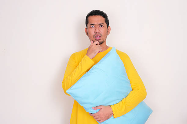 istock Adult Asian man holding a pillow showing confused face expression 2229468366