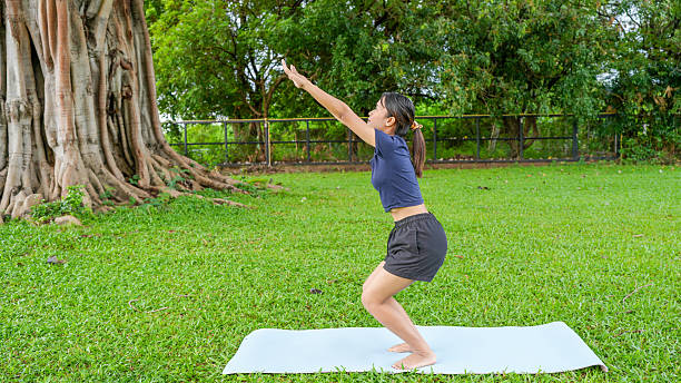 istock Woman performs yoga pose outdoors on white mat, surrounded by lush green grass and large tree. scene conveys tranquility and focus, highlighting connection between nature and physical well being 2229468772
