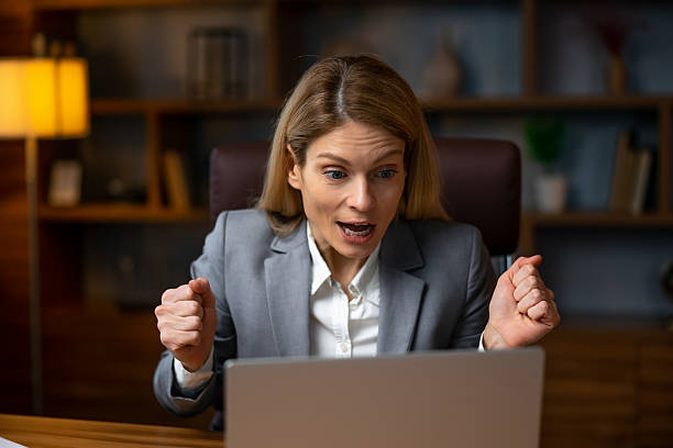 istock Excited  woman raising her arms while working on her laptop - su 2229487004