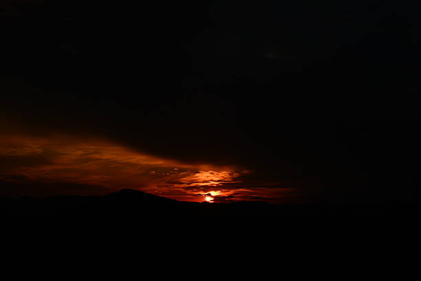 The setting sun paints the sky in fiery red hues, illuminating dramatic clouds with a breathtaking glow as day transitions into twilight.