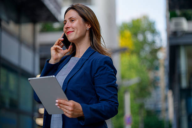 istock Professional woman networking, using tablet and smartphone near modern corporate skyscrapers during workday 2229496782