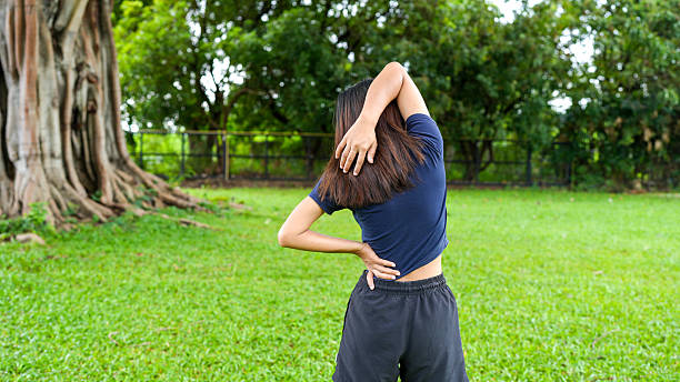 istock Young woman stretches her back while standing lush green park, surrounded by trees. scene conveys sense of relaxation and physical well being, highlighting importance of maintaining flexibility 2229501461