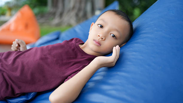 istock Young boy relaxes on blue bean bag, displaying calm expression. outdoor setting features greenery in background, creating serene atmosphere 2229501815