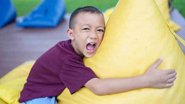 istock Joyful child expresses excitement while hugging large yellow bean bag. vibrant colors and playful setting create lively atmosphere, capturing essence of childhood fun and happiness 2229501817