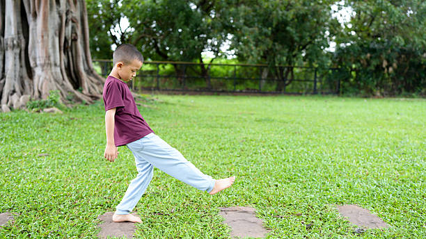 Young boy playfully balances on stone path in lush green park, showcasing joy and curiosity. serene environment enhances carefree spirit of childhood