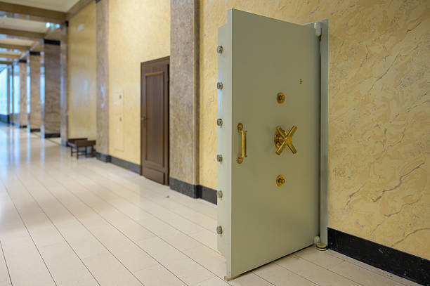 A sturdy, vintage safe door stands in a bank corridor beside polished walls.f