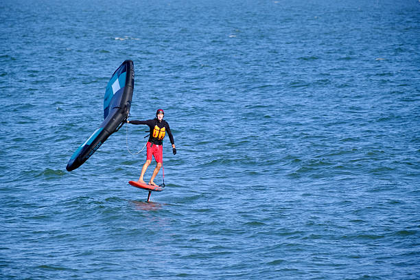 Virginia Beach, Virginia, USA August 09,2025:  On the Chesapeake Bay in Virginia Beach people take up the sport of wind surfing.  Wind surfing is a self-propelled wind sport that combines sailing and surfing.