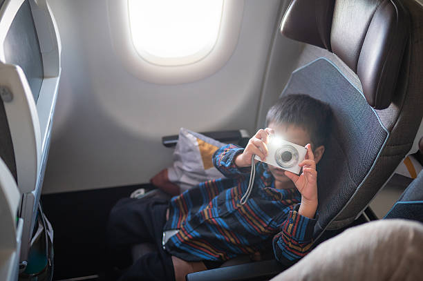 A young boy excitedly taking photos with a camera while aboard an airplane, demonstrating the spirit of discovery and adventure that comes with travel and unique experiences.