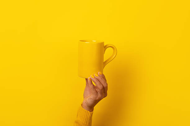 istock Hand with yellow nails and sweater holding a plain yellow mug against a seamless yellow background, creating a monochromatic look 2229512016