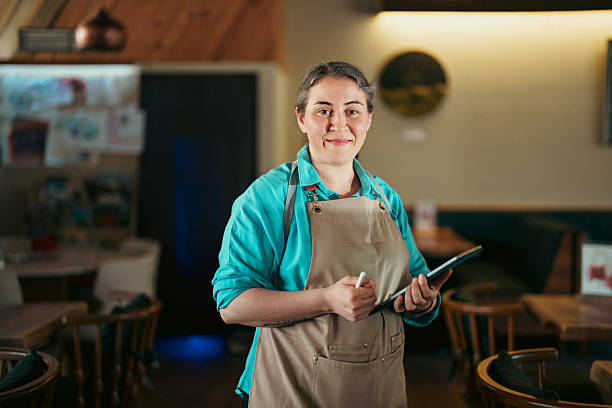 istock Restaurant Owner Walking Between Tables with Digital Tablet and Looking At The Camera 2229513644