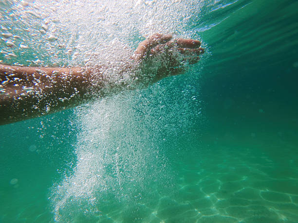 A hand underwater creating a splash and bubbles in a clear turquoise sea, with sunlight filtering through the water. Selective focus.