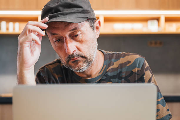 istock Man wearing camouflage army shirt and military hat using laptop computer at home 2229514519