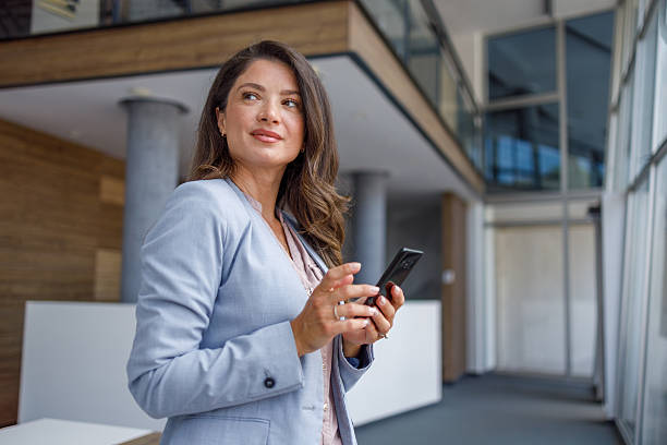 istock Businesswoman using smartphone in modern office building lobby 2229518298