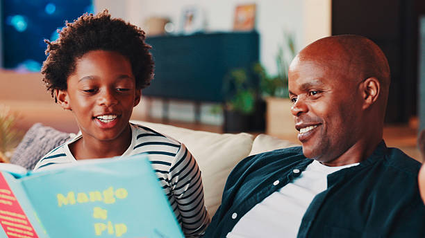 istock Black family, dad and child with book on sofa for storytelling, language development and learning support. Happy people, man and boy kid in home with fantasy novel for knowledge, reading and bonding 2229518832
