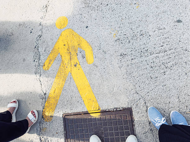 Painted yellow walking man symbol on pavement guiding pedestrian movement in urban area.\nKeywords: Venice, walking, pedestrian, man, symbol, pavement, yellow, marking, sign, city, urban, travel, guide, direction, tourism, public, concrete, commute, station, road, navigation, outdoors, step, journey, path, footpath