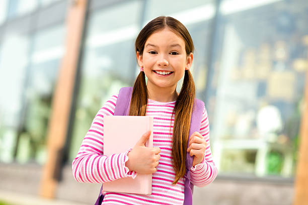 istock Smiling schoolgirl with a backpack outdoors holding a notebook, showcasing a charming and confident young student spirit on a sunny day. 2229521129