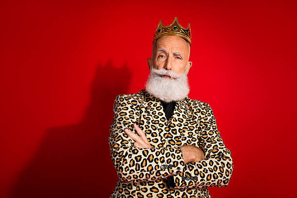 istock Stylish elderly man in leopard print suit and crown gestures confidently on red background exuding charm and charisma 2229521799
