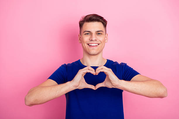 istock Young man making heart gesture with hands on pink background, symbolizing love and positivity in casual style 2229522302