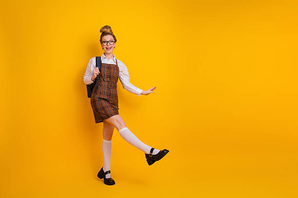 istock Young woman in school uniform posing playfully with a backpack, stylish outfit, yellow background, academic theme 2229524232