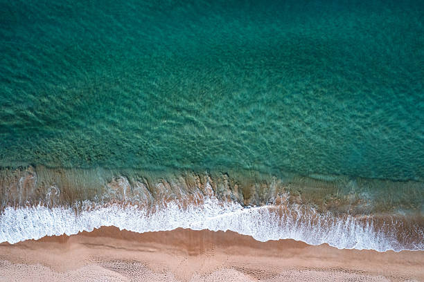 istock Idyllic, crystal clear, shallow turquoise ocean water lining a sandy shore with abstract sea foam textures from breaking waves. Captured from high above the beach. 2229527732