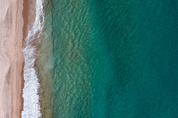 istock Idyllic, crystal clear, shallow turquoise ocean water lining a sandy shore with abstract sea foam textures from breaking waves. Captured from high above the beach. 2229527812