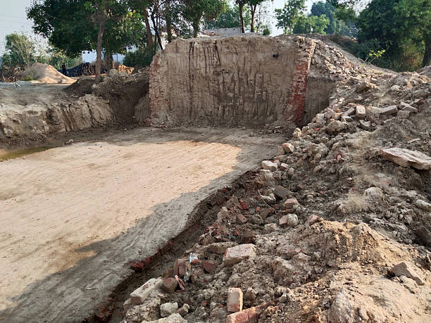 istock Small Bridge Under Construction on Village Road for Irrigation Water Flow Reflecting Rural Life and Agricultural Development with Dug Earth and Fields Under Cloudy Sky Surrounded by Houses and Green Countryside 2229530950