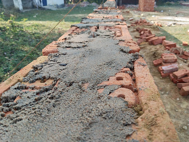 Closeup view of bricklaying process with cement mortar applied on red bricks for boundary wall construction in rural area, traditional masonry technique in Indian village construction work