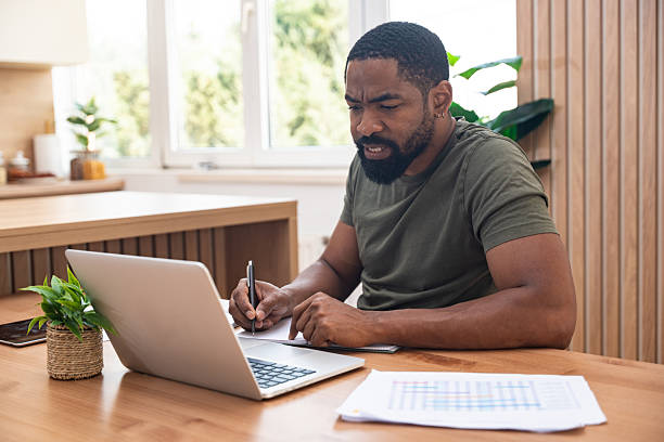 istock Millennial African American man taking notes during webinar or business meeting, using laptop, working or studying online, sitting at desk in home office. Freelance work, e-commerce startup company. 2229532277