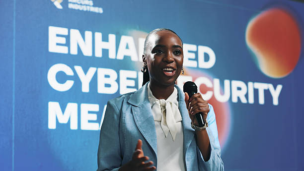 istock Happy, black woman and speaking with mic at seminar for cybersecurity presentation or tech summit. Female person, business speaker or presenter with technology for speech, online safety or campaign 2229538248
