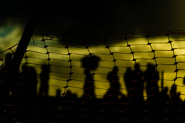 Unidentified people blurred in silhouette behind a plastic fence during a dramatic sunset. Winter season. Tourists traveling.