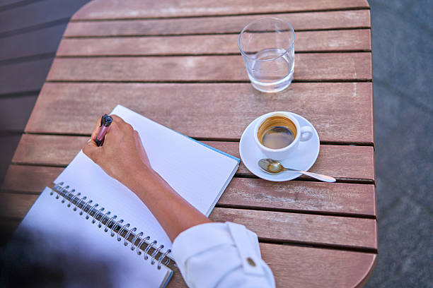 White coffee cup on wooden table with notebooks ]ans spoon on wooden table