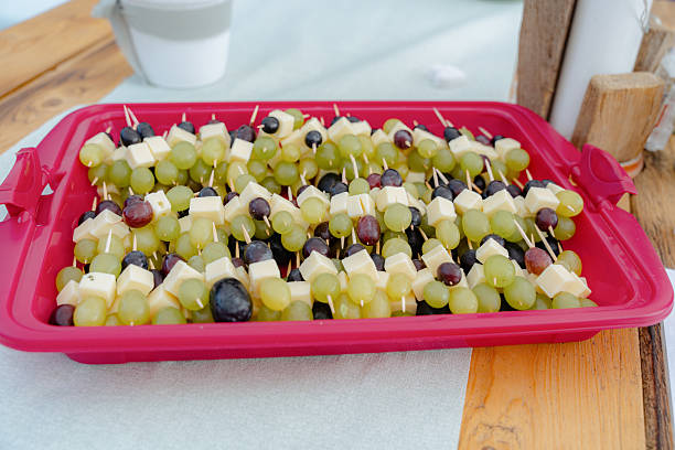 Delicious cheese and grape skewers neatly arranged on a vibrant red tray, ideal for parties or snacks. Green and black grapes paired with cheese cubes create a visually appealing platter.