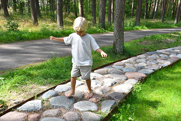 Barefoot boy walking on a sensory trail through a sunny pine forest in Lithuania