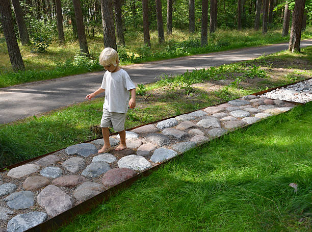 Little Barefoot boy walking on a sensory trail through a sunny pine forest in Lithuania