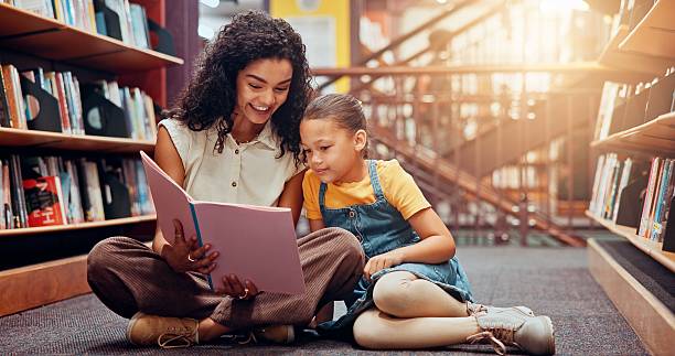 istock Child, library or teacher reading book for learning, development or storytelling in school. Teaching, tutor or woman with girl, smile or kid for literature lesson, fairy tale or education support 2229544249