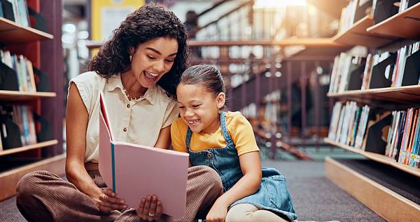 istock Kid, excited or teacher reading book for learning, development or help in school. Teaching, happy or woman with girl, smile or child in library for literature lesson, fairy tale or education support 2229544284