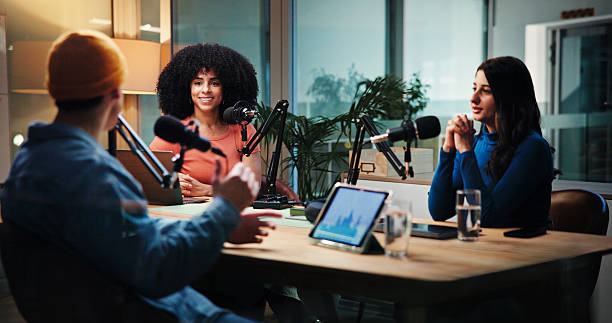 istock Podcast, talking and man with women in studio with questions for interview, discussion and conversation. Content creation, host and people with mic for recording radio show, broadcast and live stream 2229551769