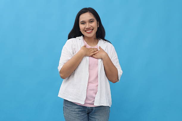 istock Young Asian woman touched happy with compliment, feeling relieved, smiling looking at camera holding chest, standing isolated on blue background. 2229555775