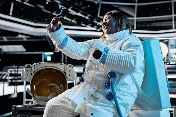 Cheerful female astronaut in starship travelling to space doing selfies using cellphone camera. Happy woman aboard orbit station having fun doing pictures on phone during cosmic journey