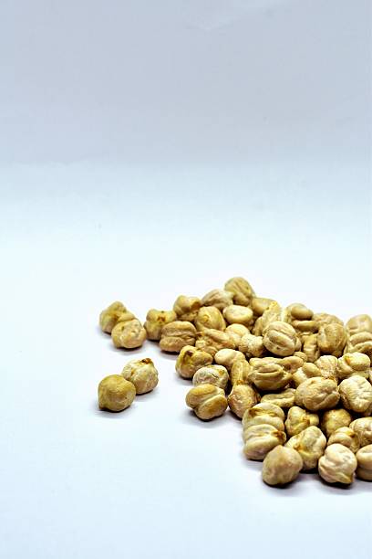 Close-up of Kabuli chana, also known as white chickpeas or garbanzo beans scattered on a wooden surface with a white background, showcasing their smooth texture and natural beige color.