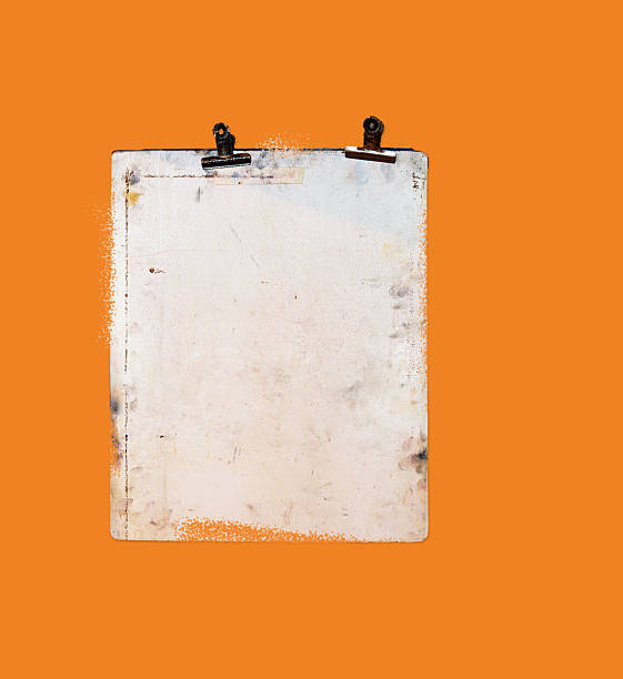 Old, weathered clipboard with dark clips centered against a vivid orange background.