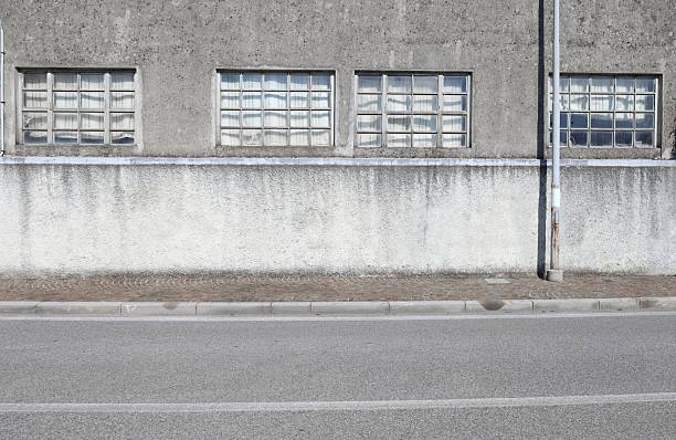 istock Concrete wall with large windows of an old mechanical workshop. Sidewalk and  road in front 2229568301