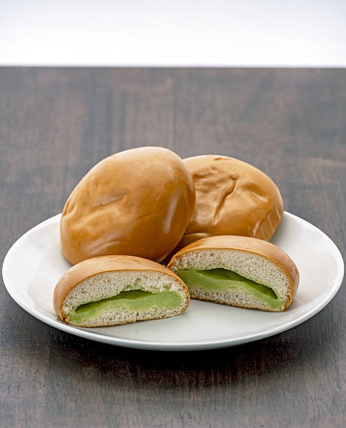 Soft bread rolls filled with creamy pandan custard are arranged on white plate, creating delicious and inviting presentation. smooth texture and vibrant green filling add touch of elegance