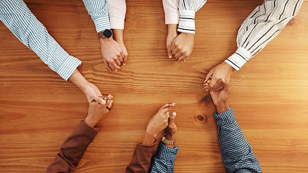istock Holding hands, collaboration and business people by table in office for synergy, unity or support. Teamwork, top view and group of corporate employees with solidarity, trust or meeting in workplace. 2229571167