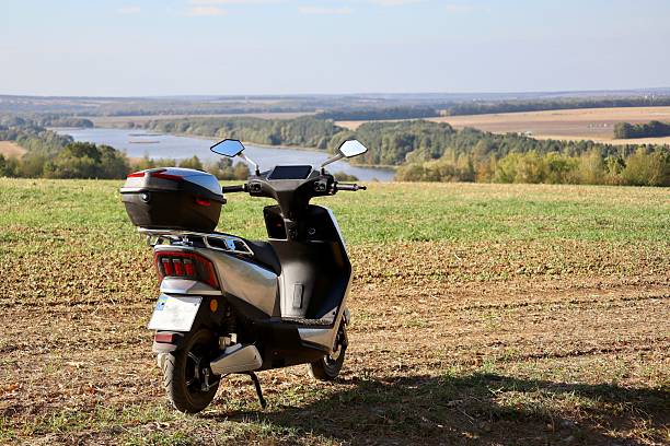 A modern scooter parked on a grassy hill overlooking a scenic landscape with fields and a river under a clear blue sky.
