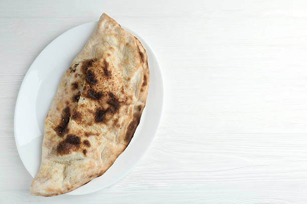 Plate with tasty calzone on white wooden table, top view. Space for text