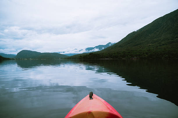 A person is kayaking on a lake surrounded by mountains on a cloudy day, enjoying the scenery and the peacefulness of nature.