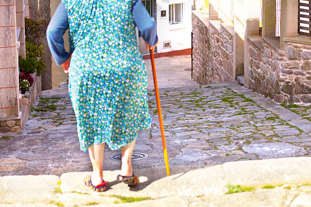 Muros village alley with old stone staircase and ramp. High angle view, street, senior woman moving down with walking cane . Muros village, A Coruna province, Galicia, Spain.