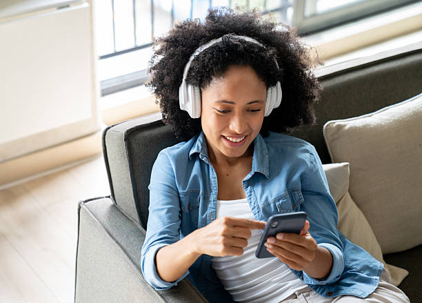 istock Woman at home using headphones while watching videos on her mobile phone 2229579803