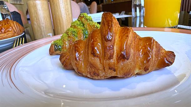 Two inviting croissants, one plain and one with pistachio, are served on a white plate, ready to be enjoyed as part of a delightful breakfast experience